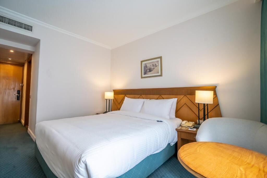 A hotel room with a large bed, two bedside tables with lamps, a wooden headboard, and a framed picture on the wall.