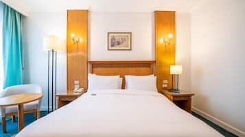 Een hotelkamer met een groot bed, twee nachtkastjes, een stoel, een bureau en een schilderij aan de muur.