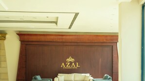 A modern hotel lobby with a plush seating area, a large wooden panel with the hotel name, and a fire extinguisher on the wall.