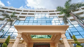 A modern hotel with a glass facade, palm trees, and a classical entrance.