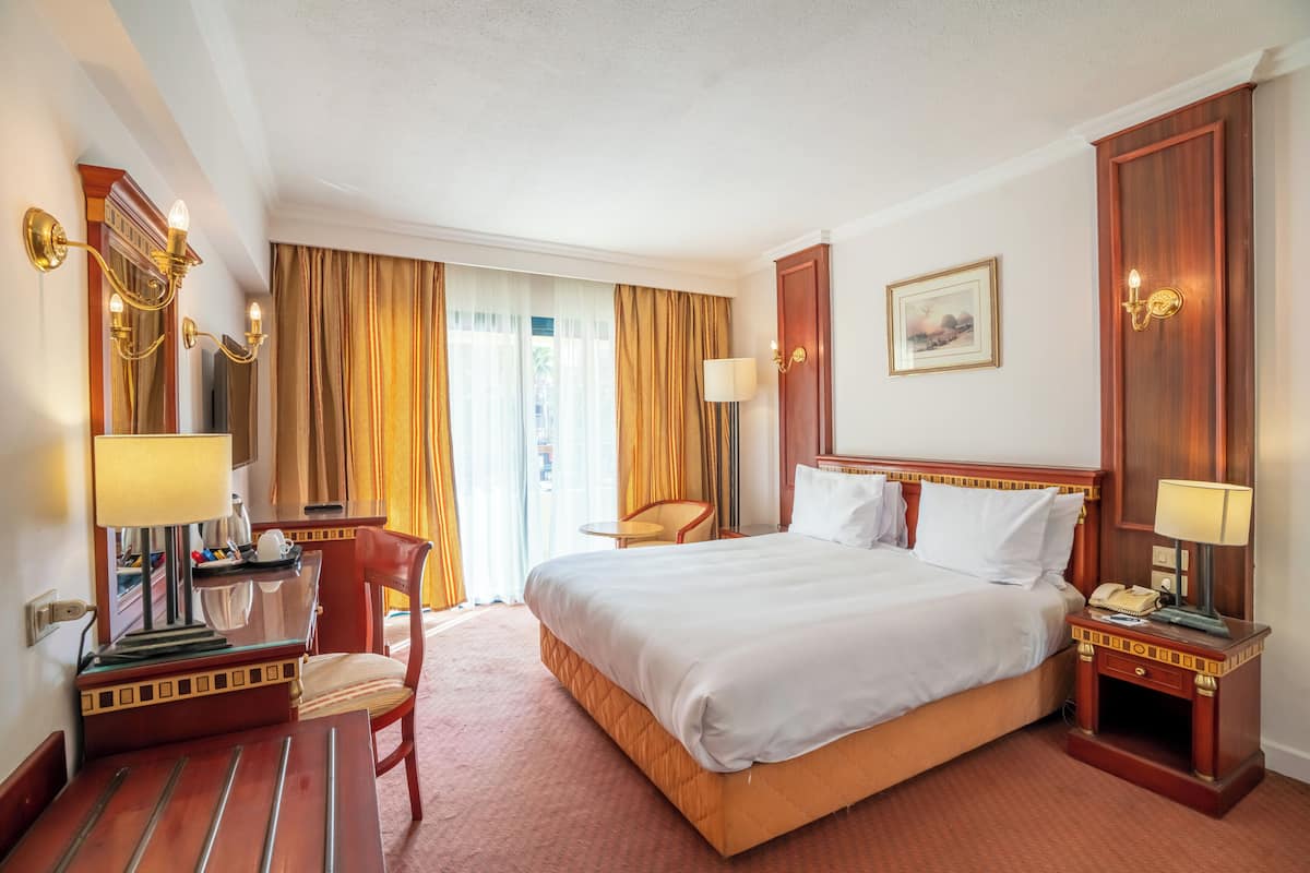 A hotel room with a large bed, a desk with a lamp, a chair, and a nightstand with a phone.