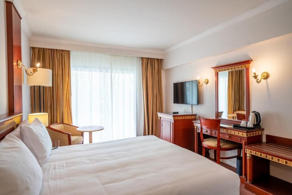 A hotel room with a large bed, a desk, a chair, a television, and a window with curtains.