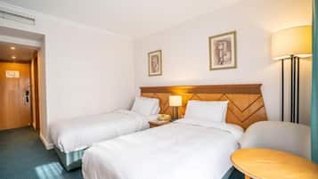 Une chambre d’hôtel avec deux lits simples, une tête de lit en bois, une table de chevet avec une lampe et une petite table ronde.