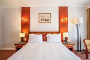 Una habitación de hotel con una cama grande, dos mesitas de noche con lámparas, un cuadro en la pared y una lámpara de pie.