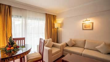 Une chambre d’hôtel avec un canapé, un fauteuil, une table à manger avec des fruits et une lampe.