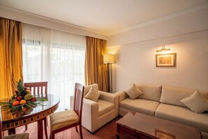 A hotel room with a sofa, armchair, dining table with fruit, and a lamp. - Azal Pyramids Hotel (Kafr ad-Dawwar)