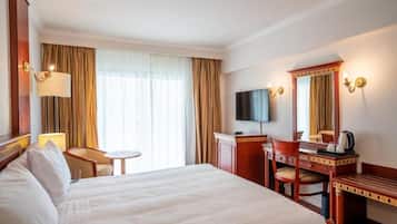 A hotel room with a large bed, a desk, a chair, a television, and a window with curtains.