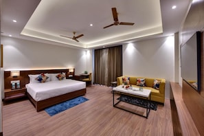 A modern hotel room with a large bed, a sofa, a coffee table, and two ceiling fans. - The Fern - An Ecotel Hotel, Alwar (Malakhera)