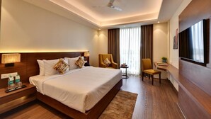 A hotel room with a large bed, bedside tables, a desk, a chair, a TV, and a ceiling fan.