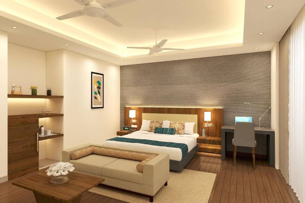 A modern hotel room with a large bed, a desk, a sofa, and a ceiling fan.