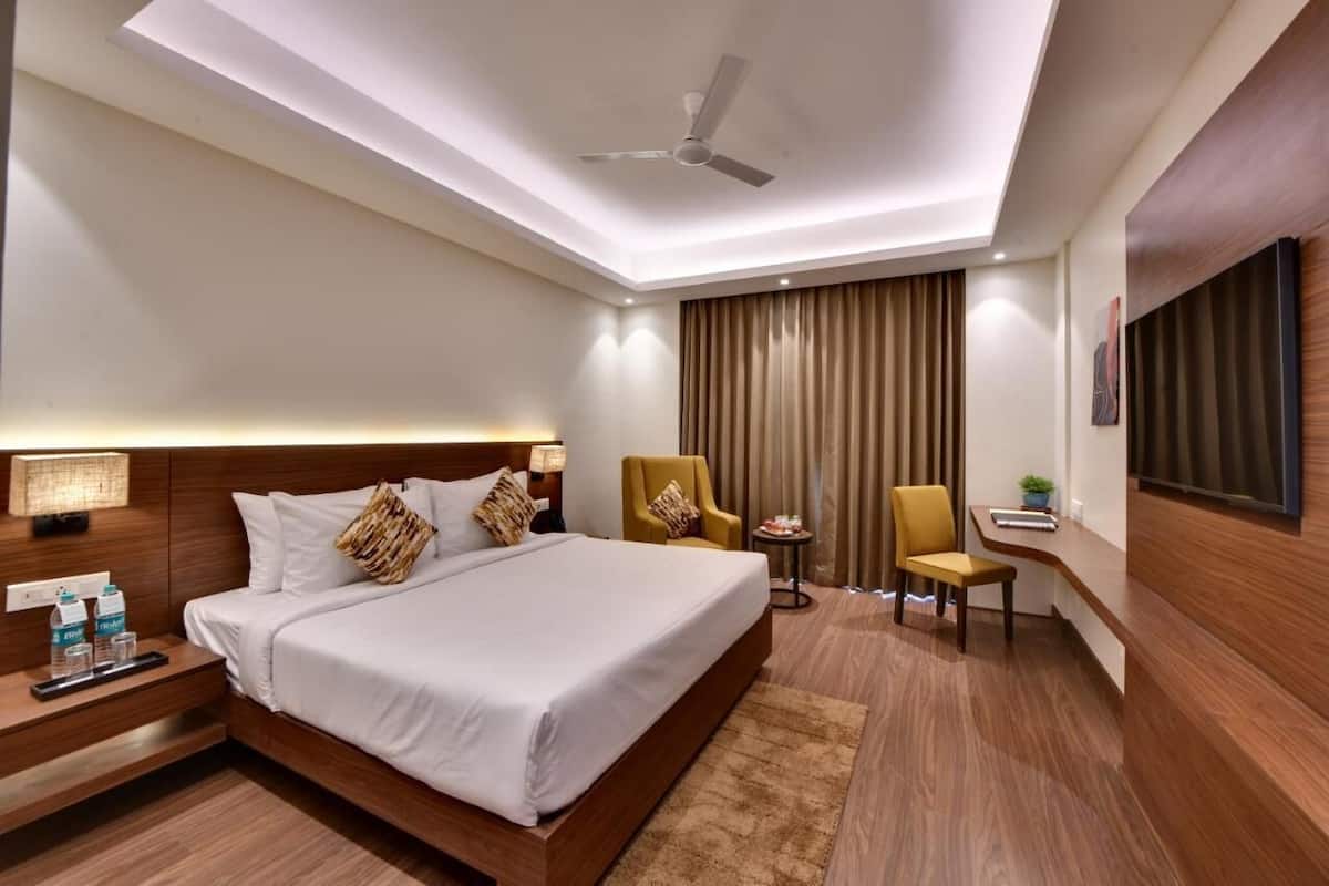 A hotel room with a large bed, bedside tables, a desk, a chair, a ceiling fan, and a TV mounted on the wall.