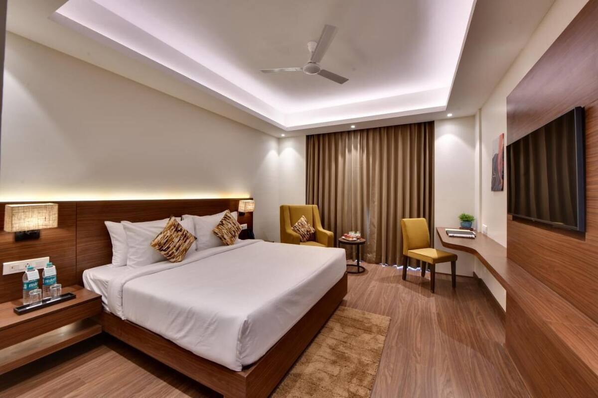 Habitación de hotel con una cama grande, mesitas de noche, un escritorio, una silla, un ventilador de techo y un televisor montado en la pared.