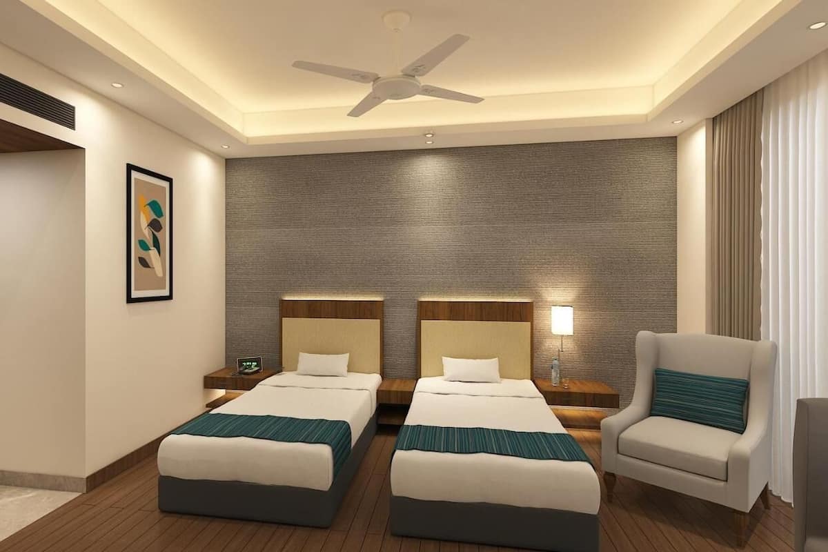 A hotel room with two beds, a ceiling fan, a nightstand with a lamp, and a chair.