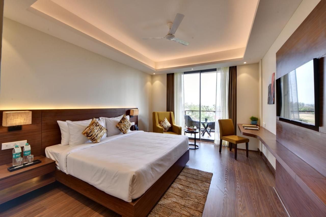 A modern hotel room with a large bed, a desk, a chair, a TV, and a balcony with a view.