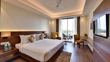 A modern hotel room with a large bed, a desk, a chair, a TV, and a balcony with a view.