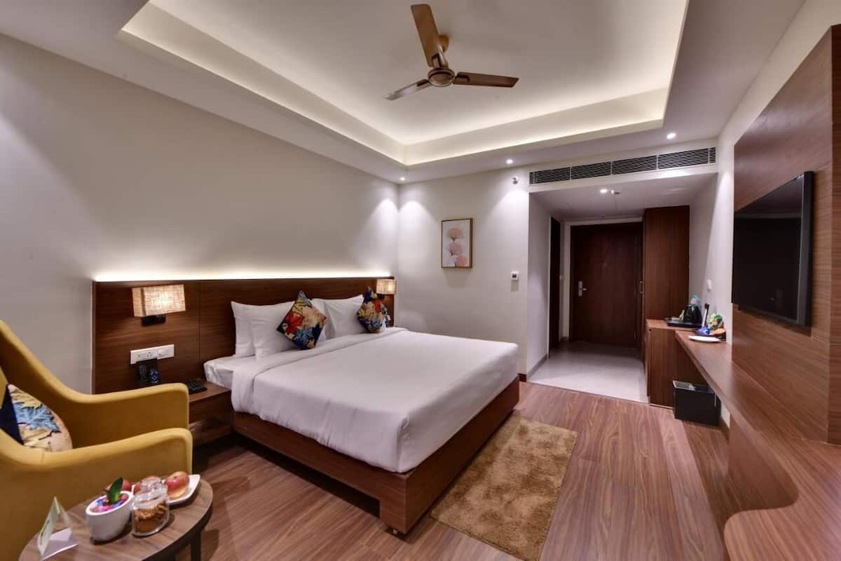 A modern hotel room with a large bed, a desk with a chair, a ceiling fan, and a TV mounted on the wall.
