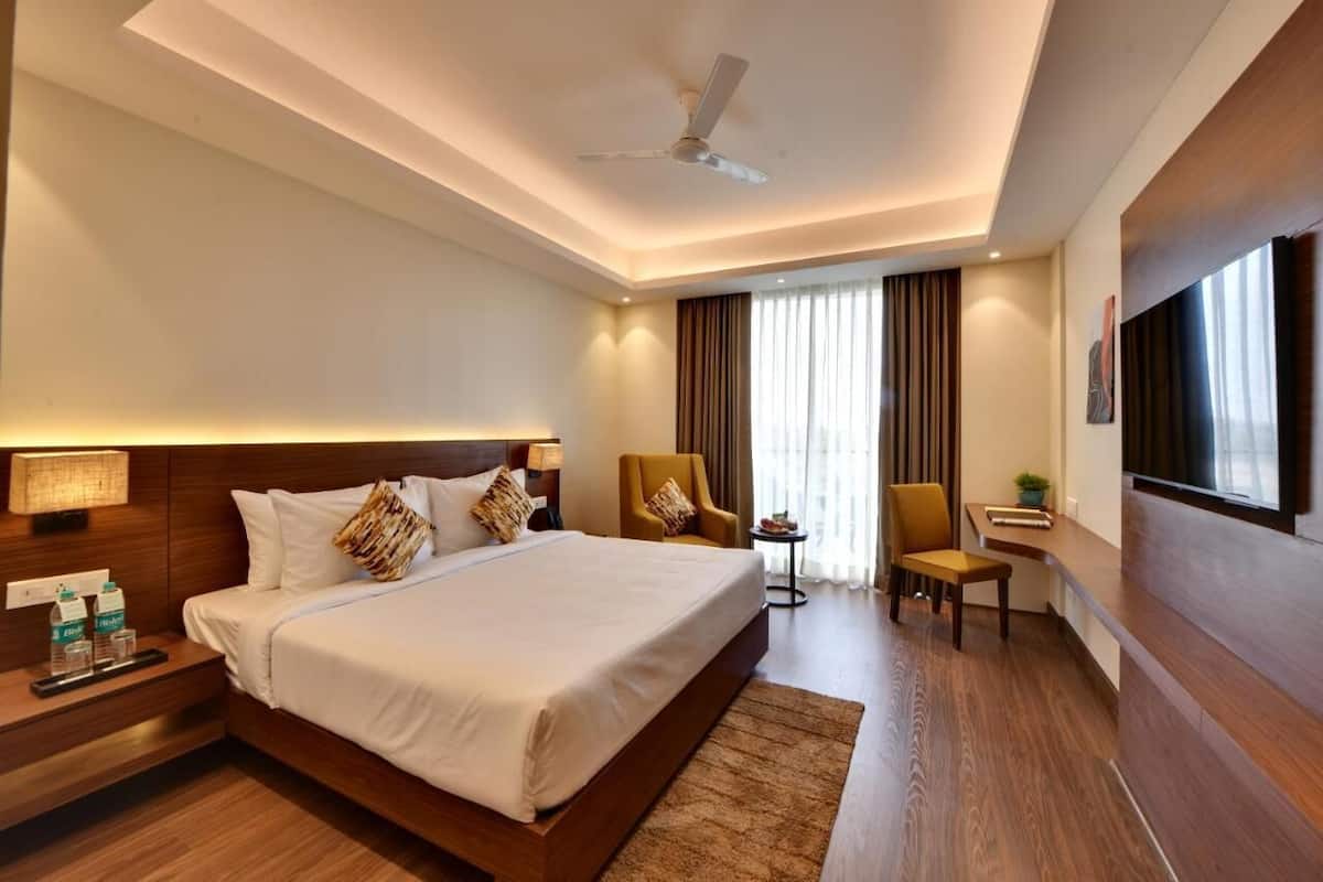 A hotel room with a large bed, bedside tables, a desk, a chair, a TV, and a ceiling fan.