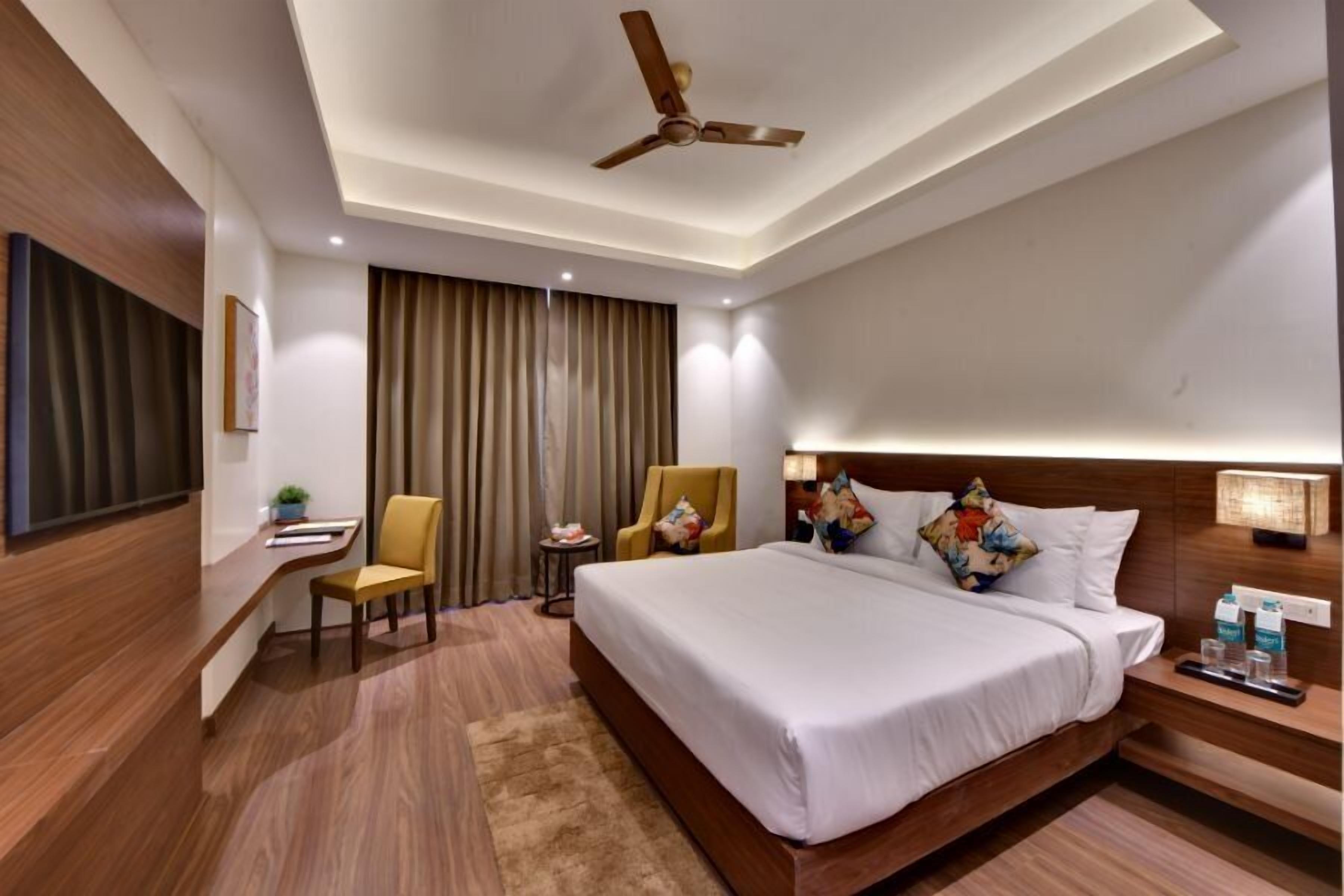 A hotel room with a large bed, a desk, a chair, a ceiling fan, and a TV.