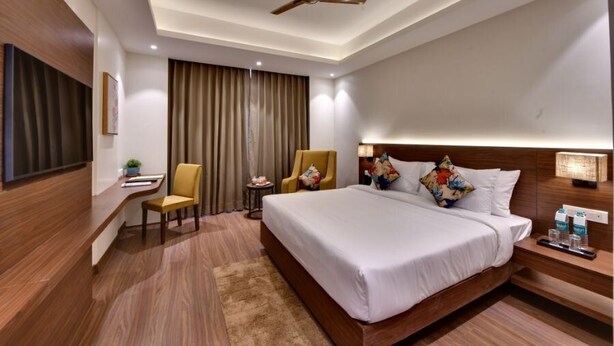 A hotel room with a large bed, a desk, a chair, a ceiling fan, and a TV.