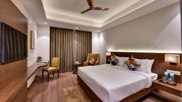A hotel room with a large bed, a desk, a chair, a ceiling fan, and a TV.