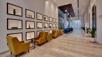 A modern lobby with framed artwork on the walls, a row of yellow chairs, and a marble floor.
