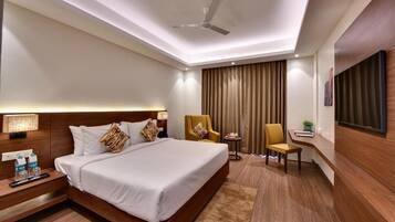 A hotel room with a large bed, bedside tables, a desk, a chair, a ceiling fan, and a TV mounted on the wall.