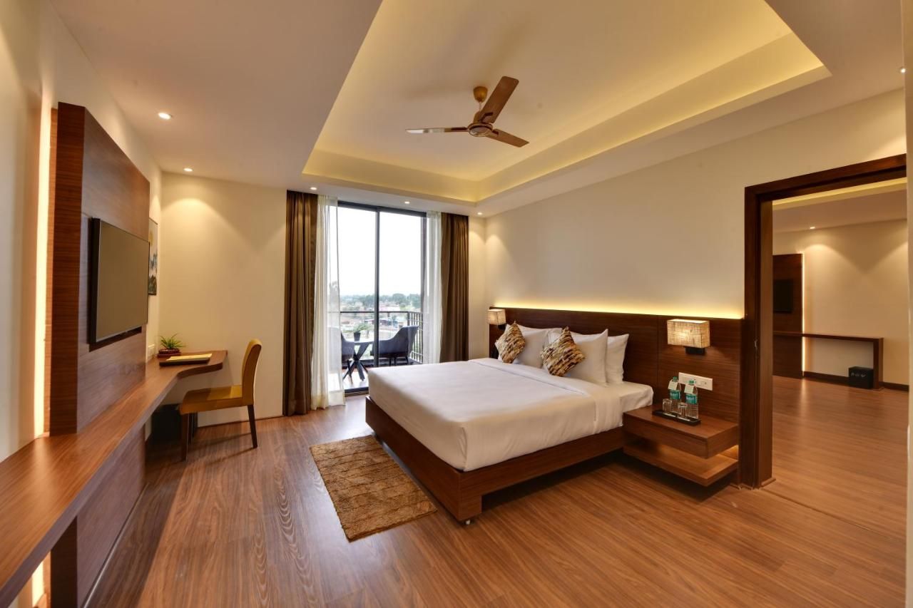 A modern hotel room with a large bed, a desk, a chair, a TV, a ceiling fan, and a view of the city.