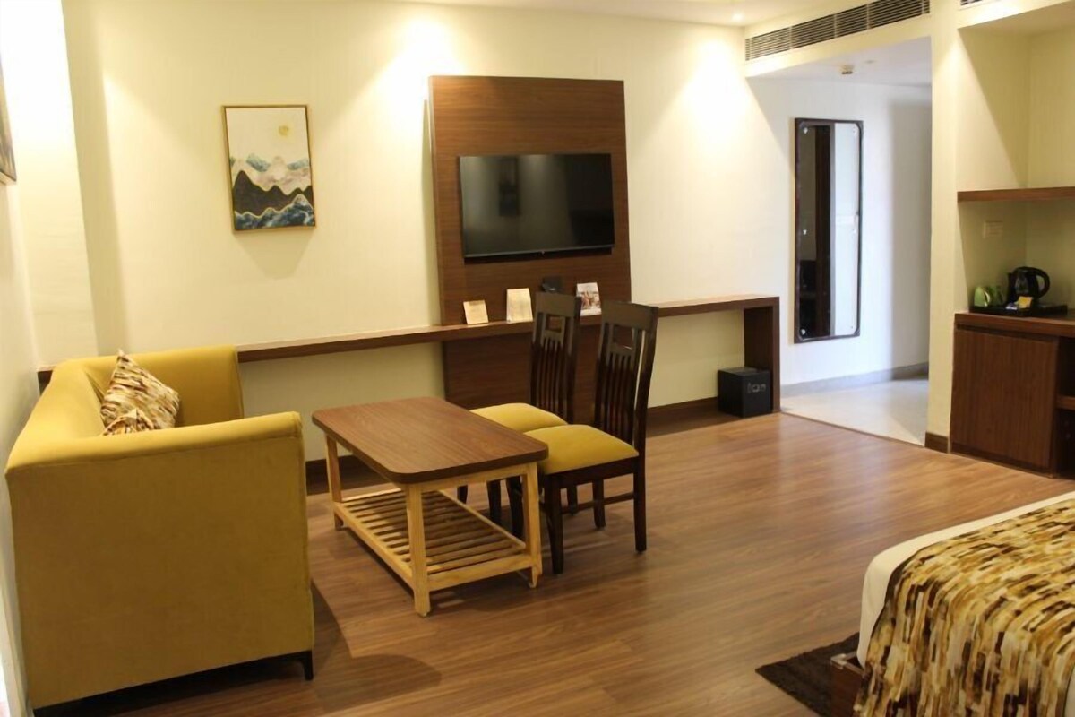 Habitación de hotel con sofá, una mesita, televisión instalada en un panel de madera y cama con colcha estampada.