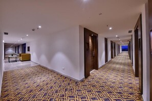 A hotel hallway with patterned carpet, recessed lighting, and a sofa.