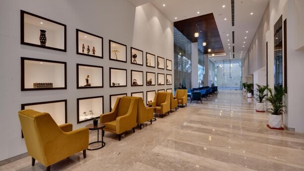 A modern lobby with framed artwork on the walls, a row of yellow chairs, and a marble floor.