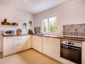 Een moderne keuken met witte kastjes, een houten aanrecht, een inbouwoven en een raam met uitzicht op groen.