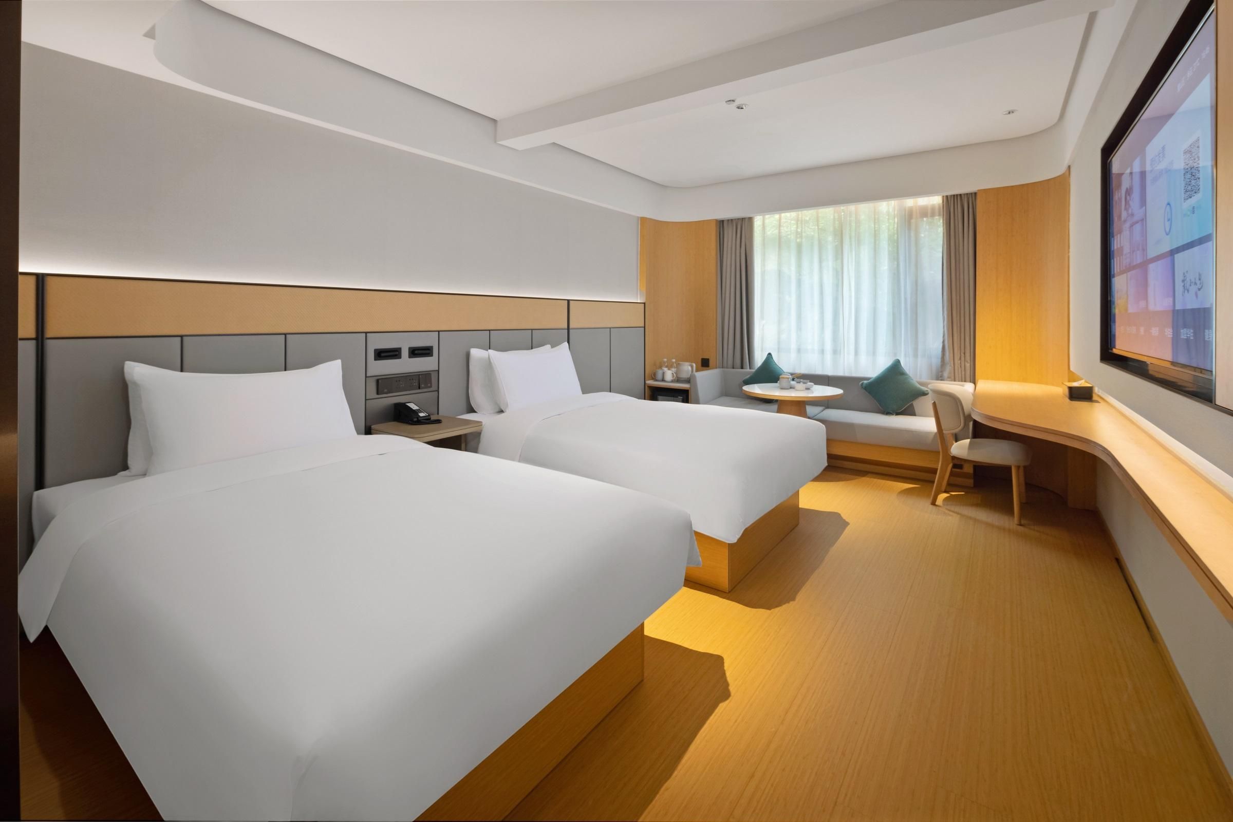 A hotel room with two beds, a desk, a chair, a TV, and a window with curtains.
