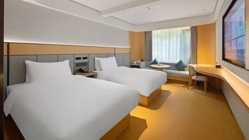 A hotel room with two beds, a desk, a chair, a TV, and a window with curtains.