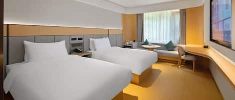A hotel room with two beds, a desk, a chair, a TV, and a window with curtains.