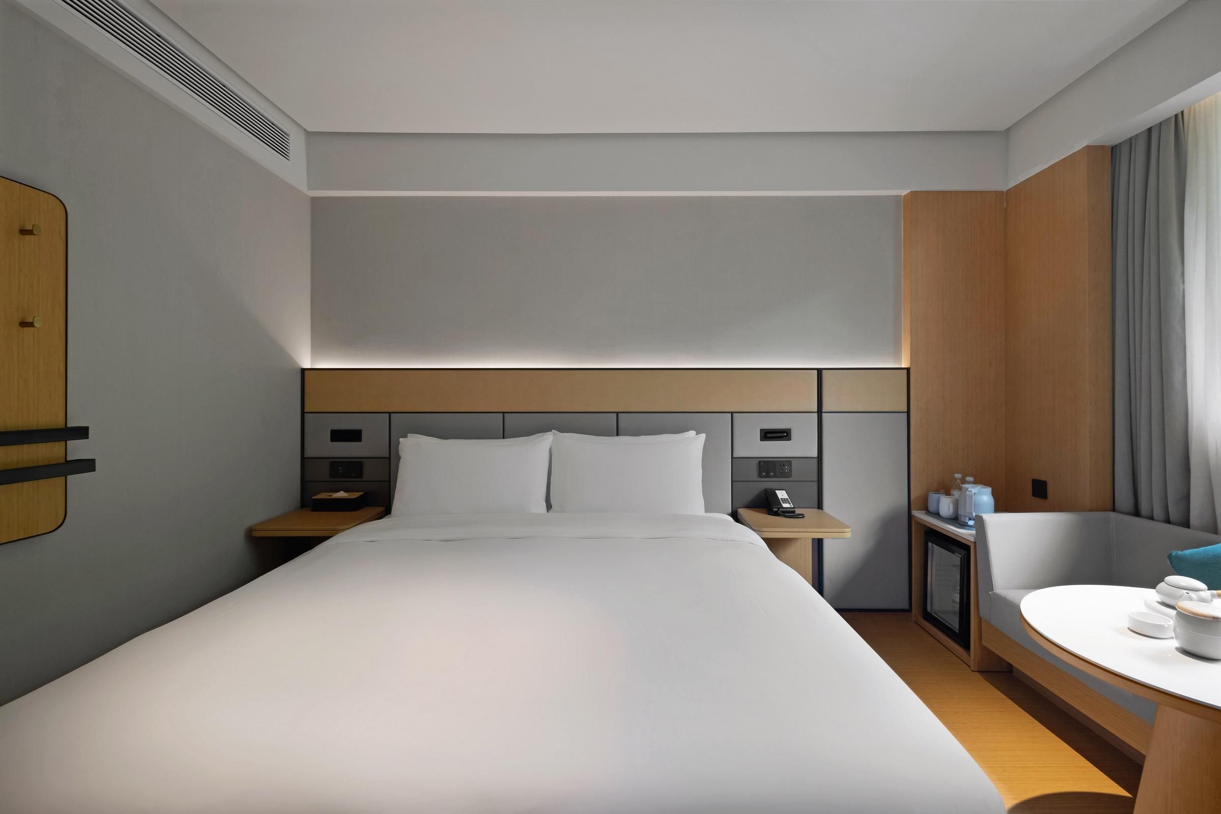A hotel room with a large bed, bedside tables, a desk, a chair, and a window with curtains.