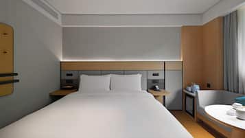 A hotel room with a large bed, bedside tables, a desk, a chair, and a window with curtains.