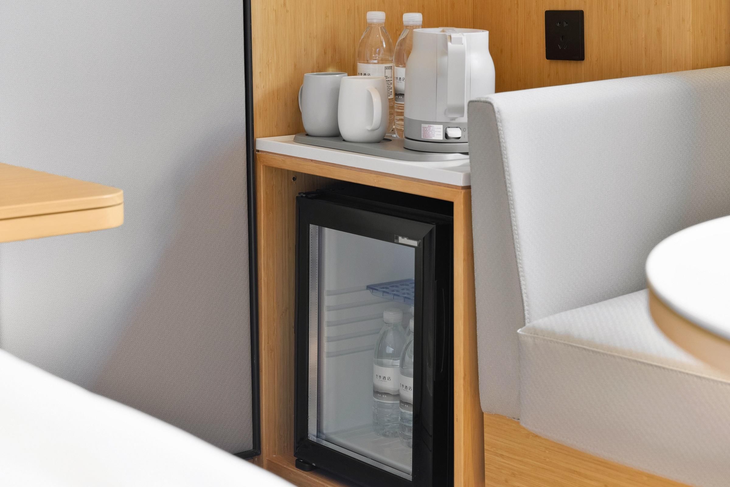 A compact kitchenette with a refrigerator, a coffee maker, and two water bottles on the counter.