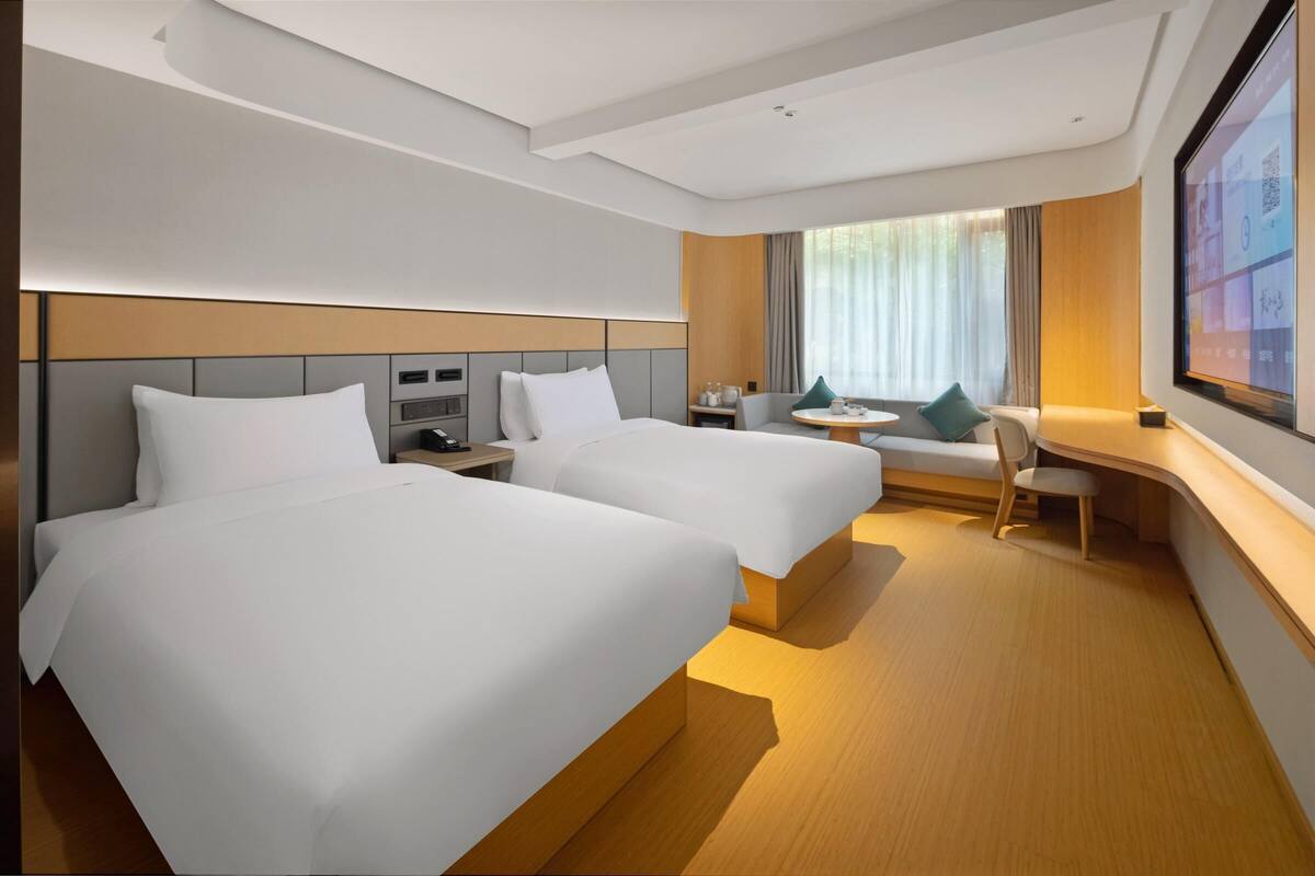 A hotel room with two beds, a desk, a chair, a TV, and a window with curtains.
