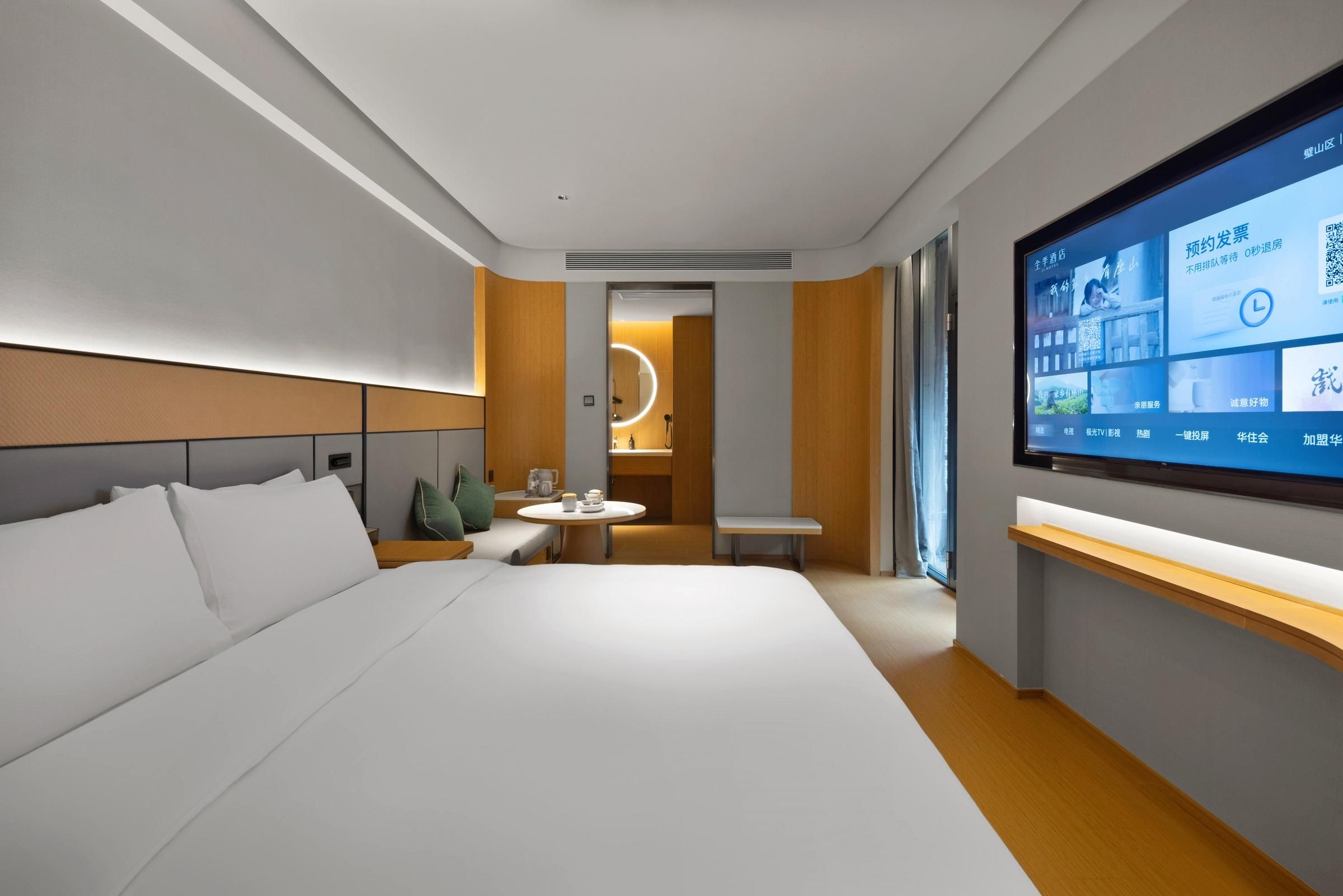 Quarto de hotel moderno com uma cama grande, TV, uma mesinha e área de estar.