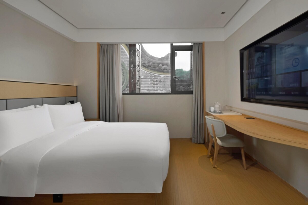 Ein Hotelzimmer mit Bett, Schreibtisch, Stuhl, Fernseher und einem Fenster mit Blick auf traditionelle Architektur.