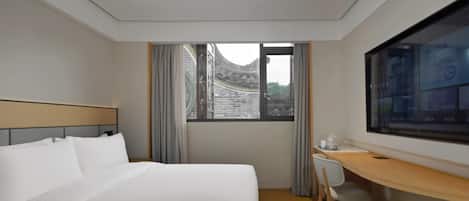 A hotel room with a bed, a desk, a chair, a TV, and a window with a view of traditional architecture.