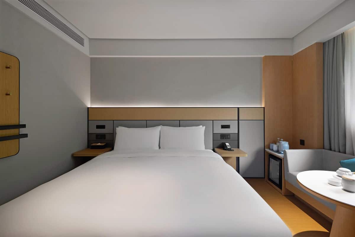 A hotel room with a large bed, bedside tables, a desk, a chair, and a window with curtains.