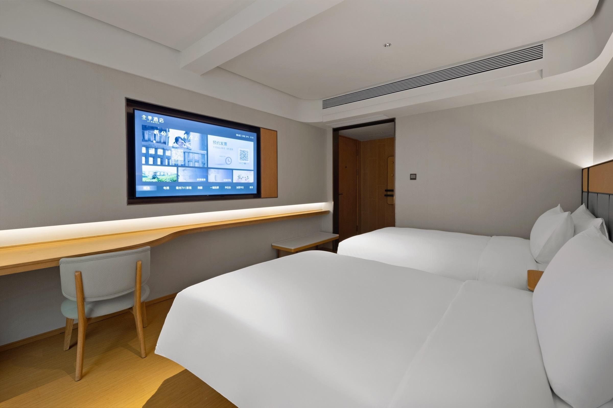 A modern hotel room with a large bed, a desk, a chair, and a TV mounted on the wall.