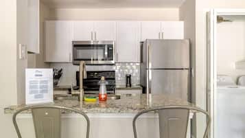 A modern kitchen with white cabinets, stainless steel appliances, and a central island with two bar stools.