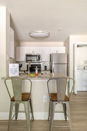 A modern kitchen with white cabinets, stainless steel appliances, and a central island with two bar stools.