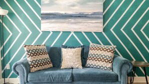 A room with a chevron-patterned wall, a blue sofa with patterned cushions, and a landscape painting above.