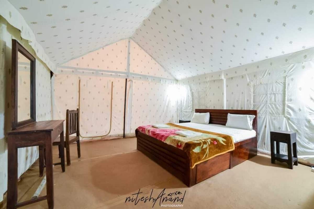 A tent-style room with a bed, a chair, a small table, and curtains.