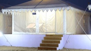Une tente avec le numéro « 104 » sur la porte, un ensemble de marches en bois menant à l’entrée et une petite table à l’intérieur.