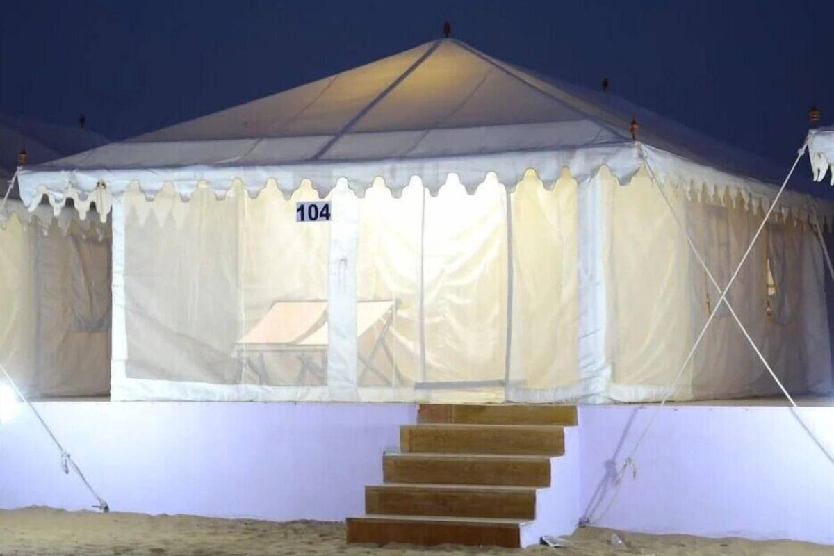 A tent with a number '104' on the door, a set of wooden steps leading to the entrance, and a small table inside.
