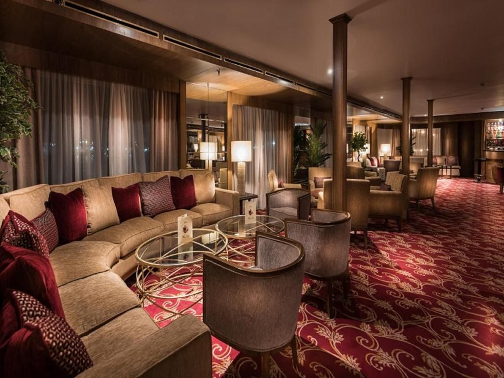 Un vestíbulo de hotel con un sofá curvo, mesas redondas y una alfombra estampada.